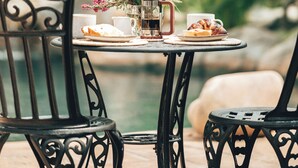 A table set with a coffee pot, cups, and pastries, surrounded by chairs, with a natural backdrop. - Villa Chad Luxury Guesthouse (Kleinmond)