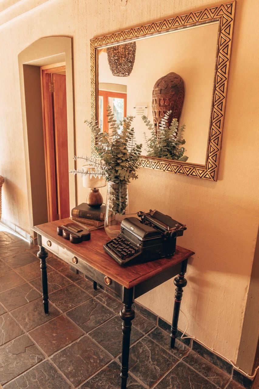 A wooden desk with a typewriter, books, and a vase with greenery.