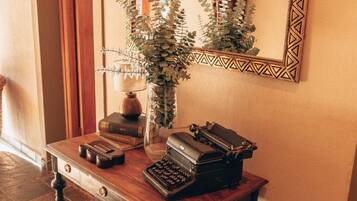 A wooden desk with a typewriter, books, and a vase with greenery.