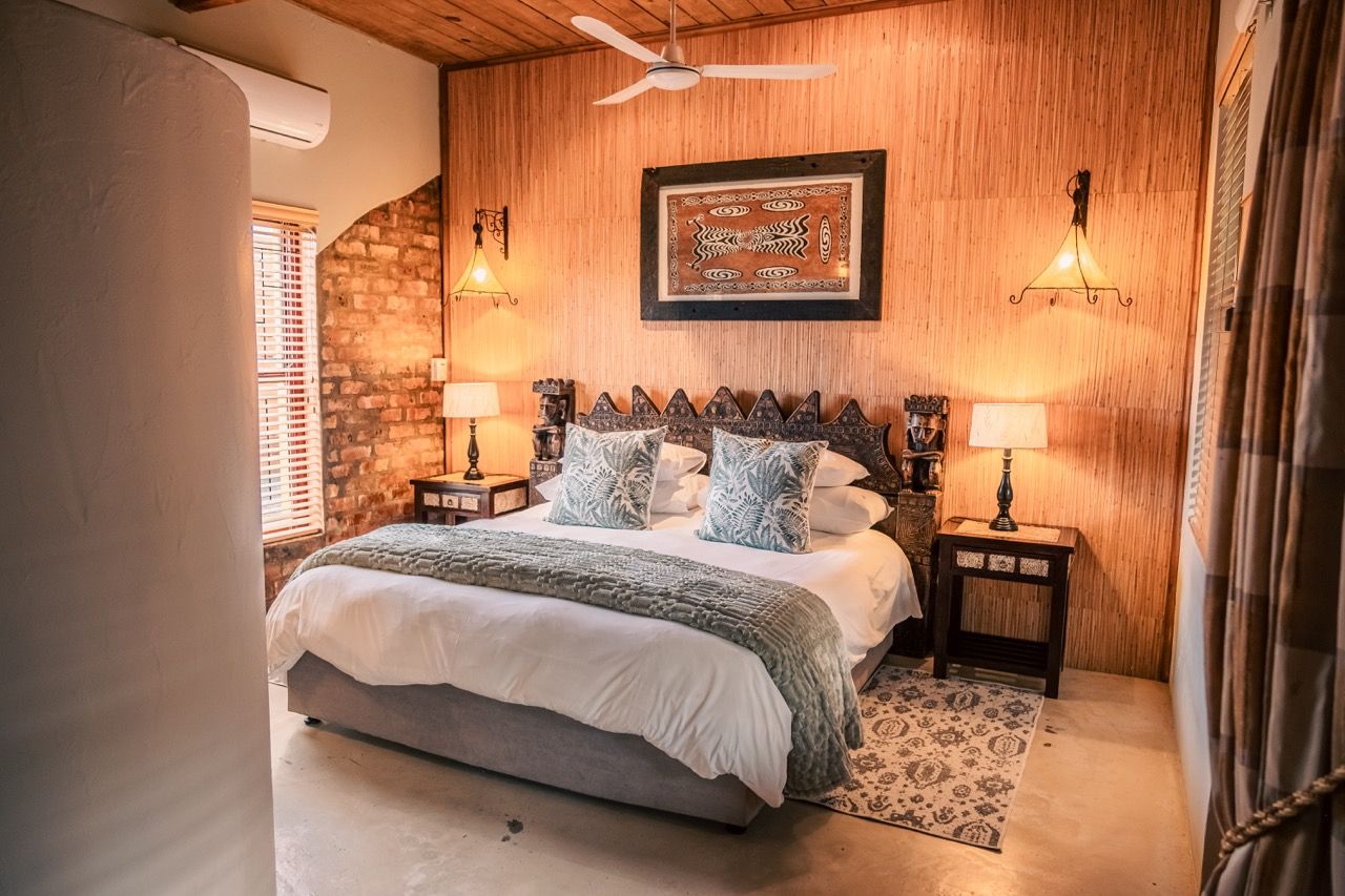 A bedroom with a wooden headboard, a bed with a white comforter, two bedside lamps, and a patterned rug.