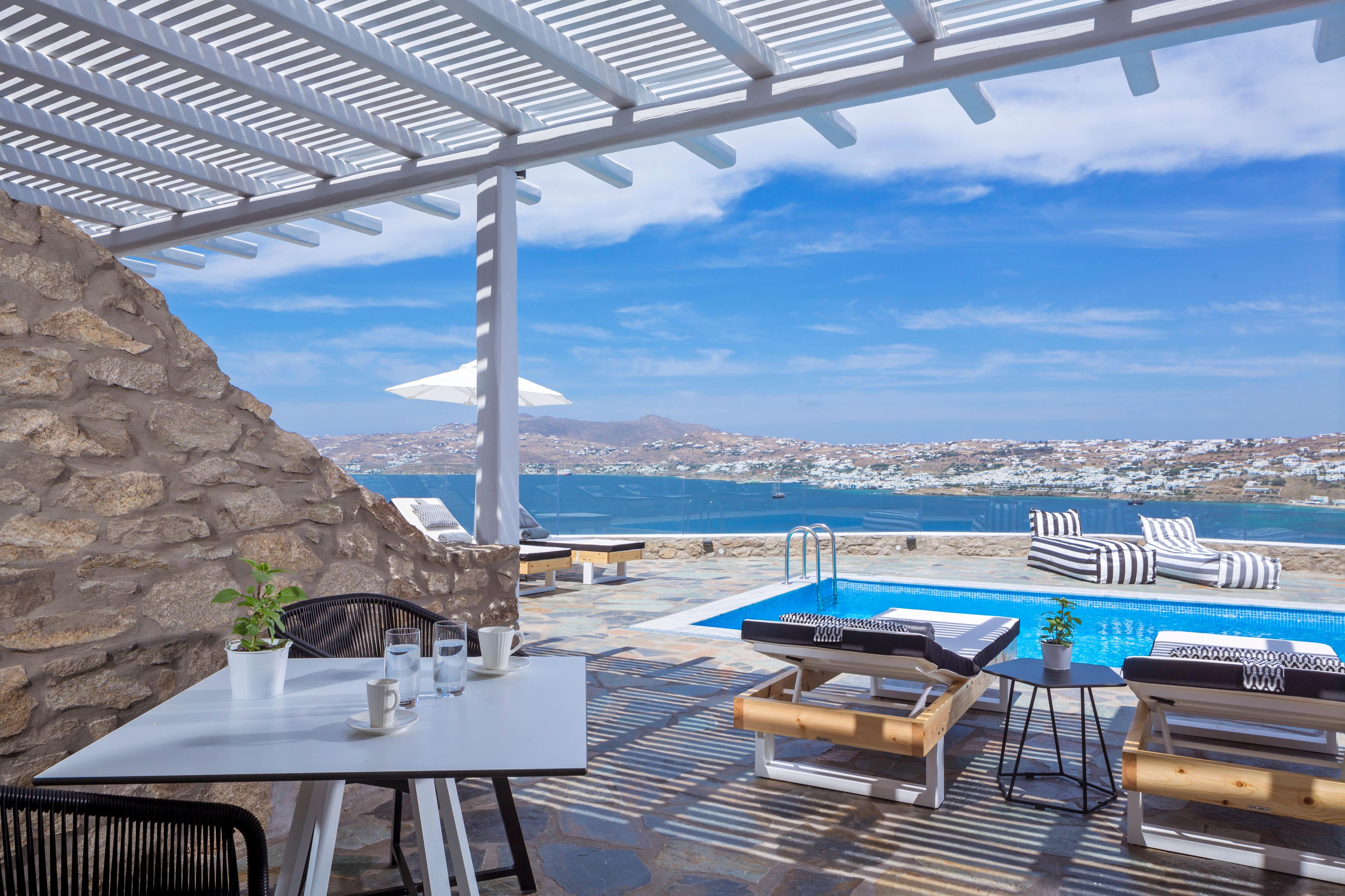 Un espace extérieur aménagé avec des sièges, une piscine, un mur en pierre et une vue sur la mer et la ville.