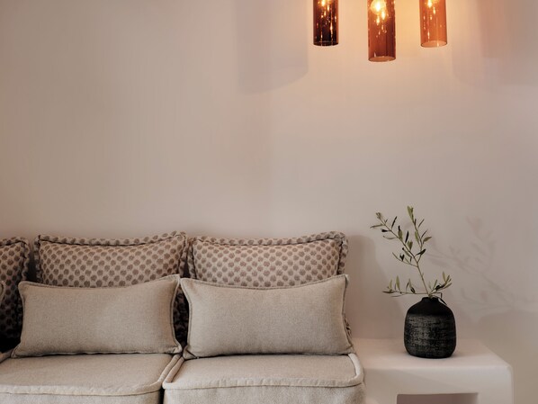 A sofa with patterned cushions, a vase with a plant, and wall-mounted lighting. - Mykonos No5 (Mykonos)