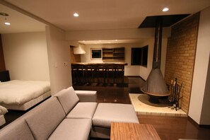 Een moderne hotelkamer met een bank, een houten tafel, een keukenhoek met een bar en een open haard.