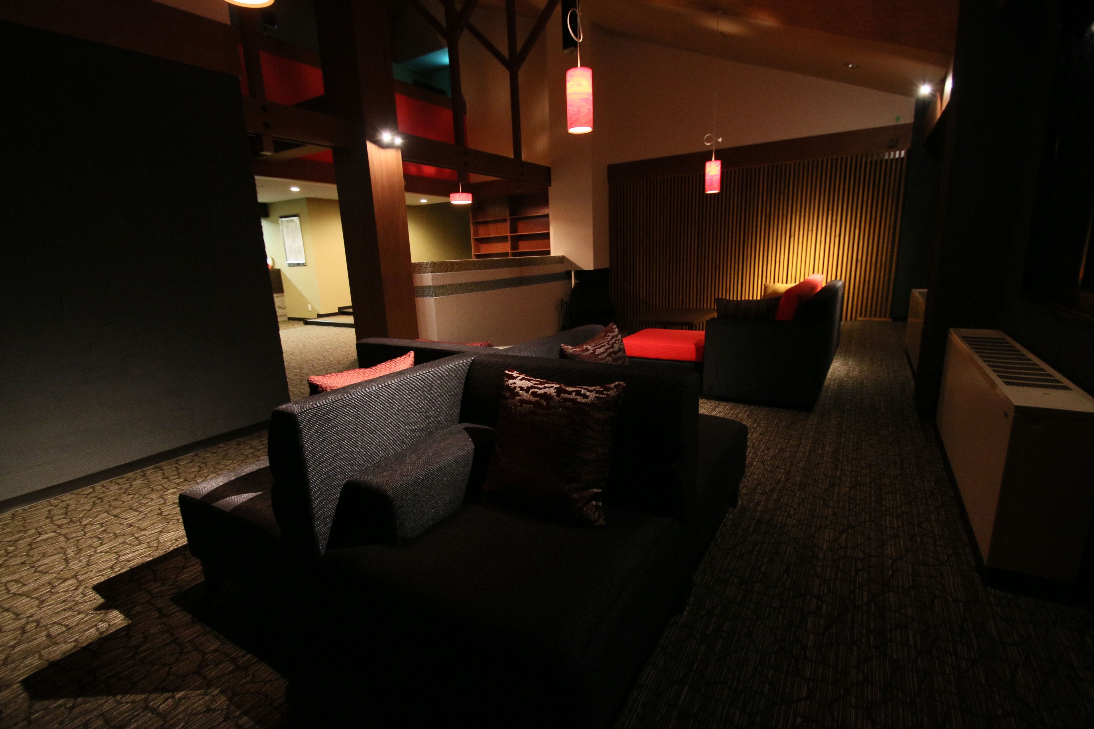 A dimly lit lounge area with a sofa, a red accent wall, and a wooden slat partition.