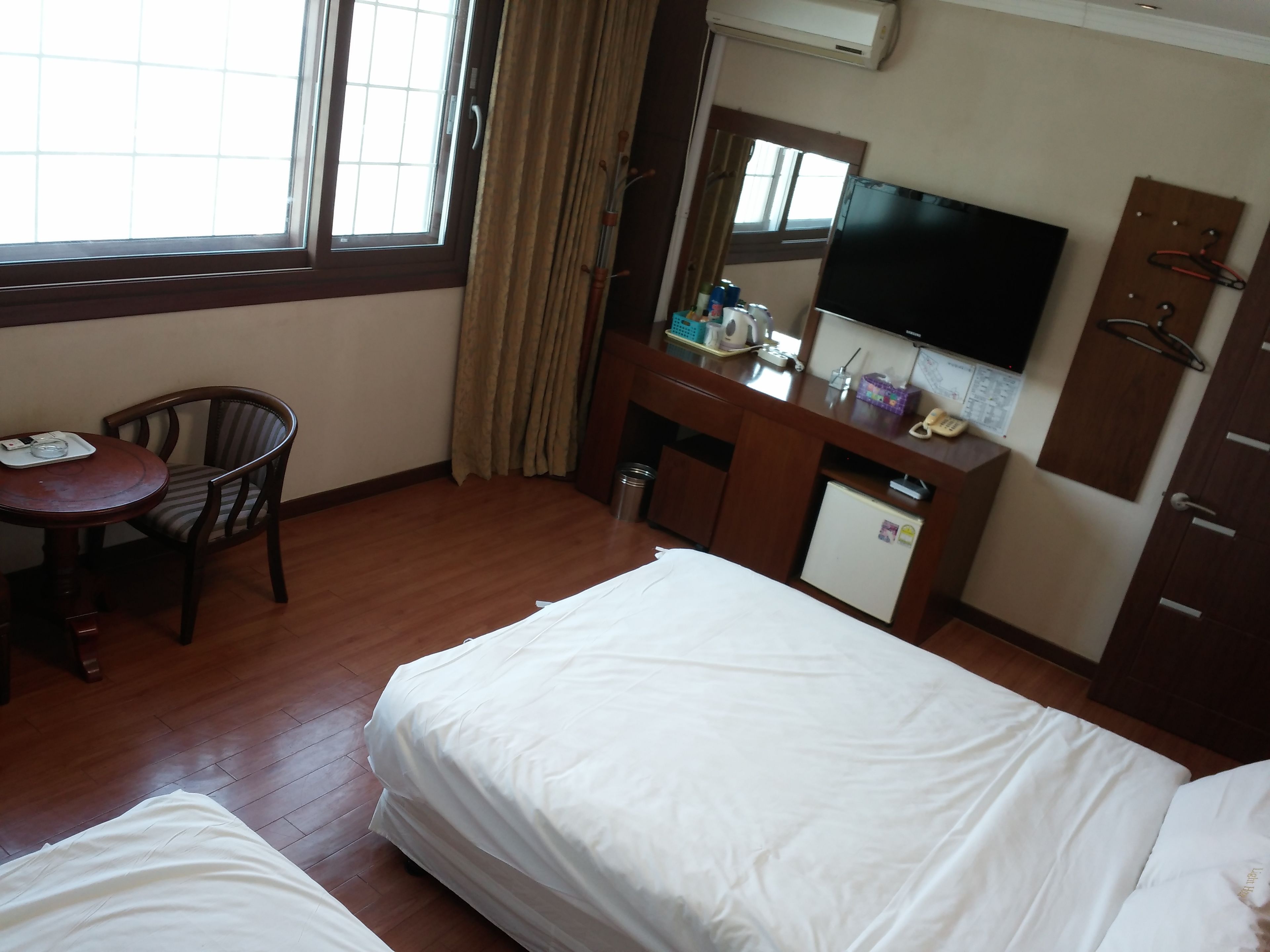 Una habitación de hotel con dos camas, un escritorio con silla, televisión y un refrigerador pequeño.