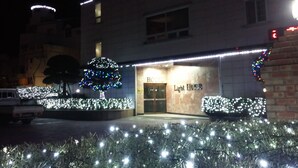 Entrada de hotel con un letrero que dice "Light House" y árboles y arbustos iluminados.