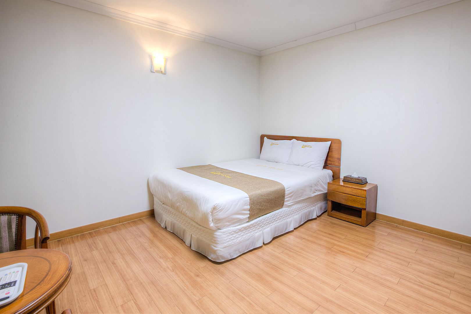 Una habitación de hotel ordenada con una cama, una mesita de noche y una pequeña silla de madera.