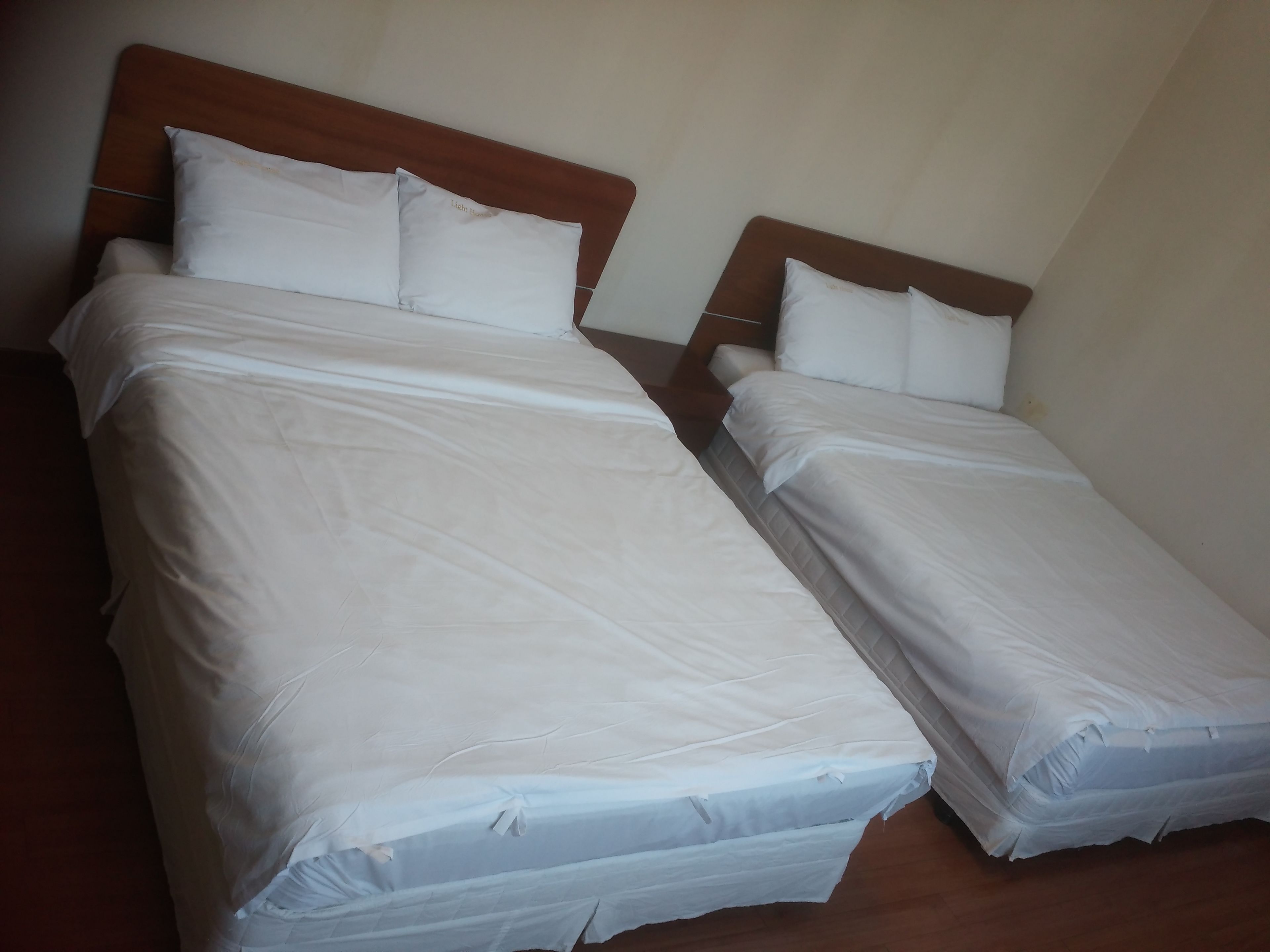 Two twin beds with wooden headboards and white bedding, arranged in a simple room with a wooden floor.