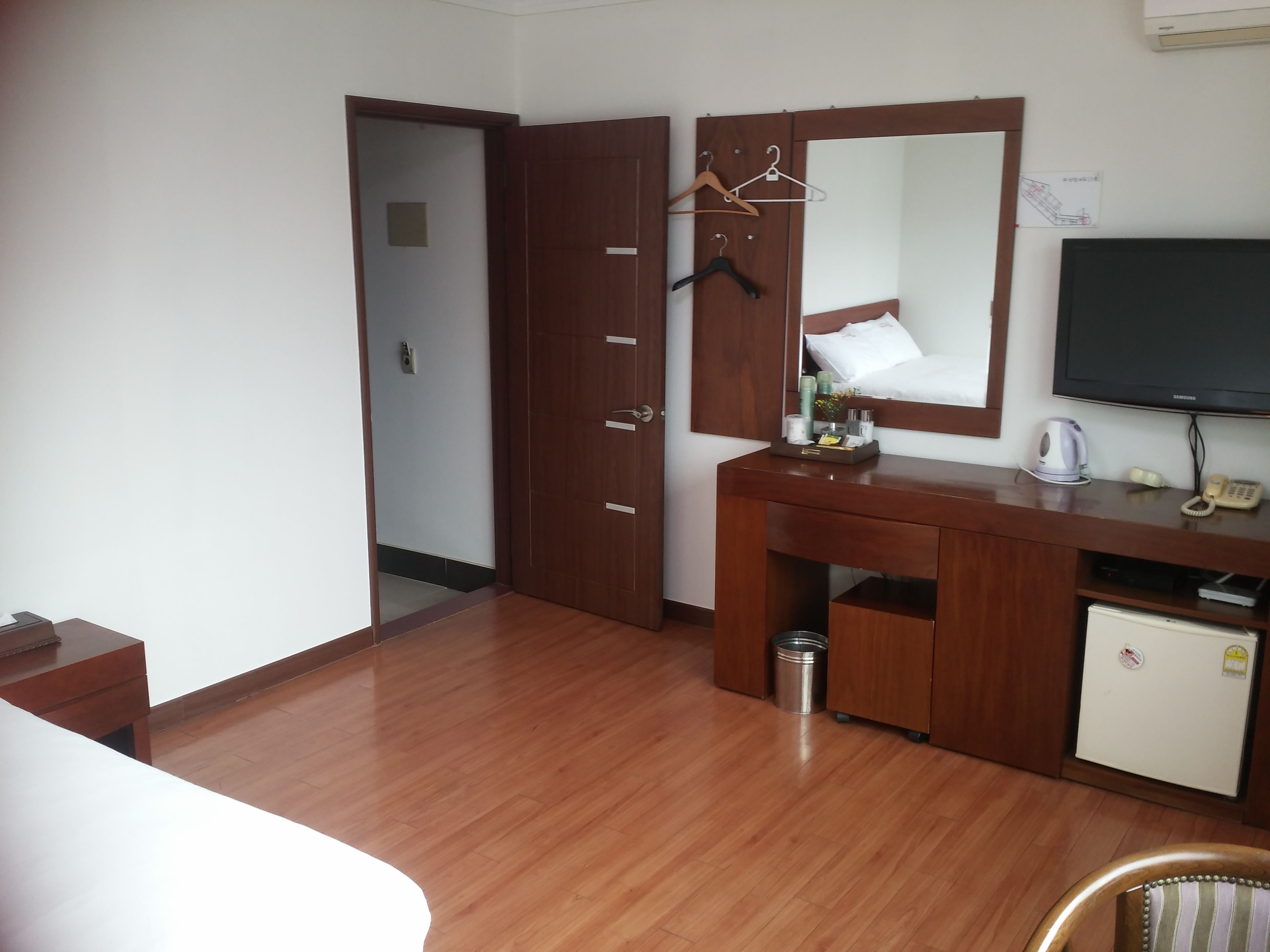 Una habitación de hotel con un escritorio de madera, un espejo, un televisor y un refrigerador pequeño.