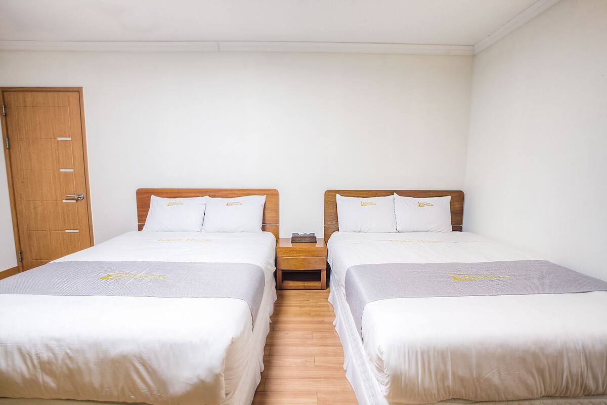 A hotel room with two single beds, wooden headboards, white bedding, and a wooden wardrobe.