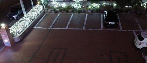 Un estacionamiento con pavimento de ladrillo, espacios de estacionamiento delimitados y una pequeña área ajardinada con luces blancas.