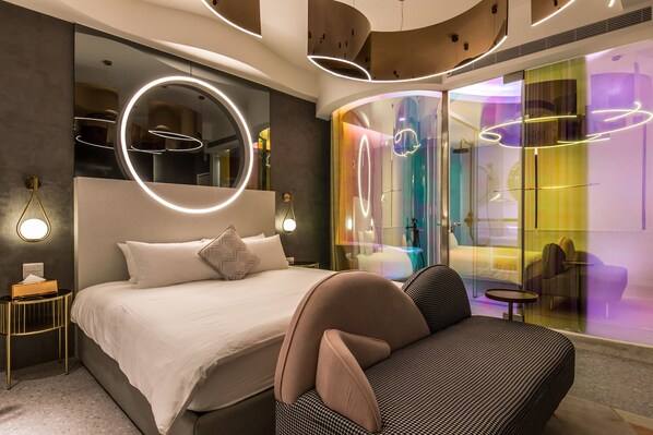 Ett modernt hotellrum med en stor säng, en soffa och en vägg av glas som avgränsar rummet.