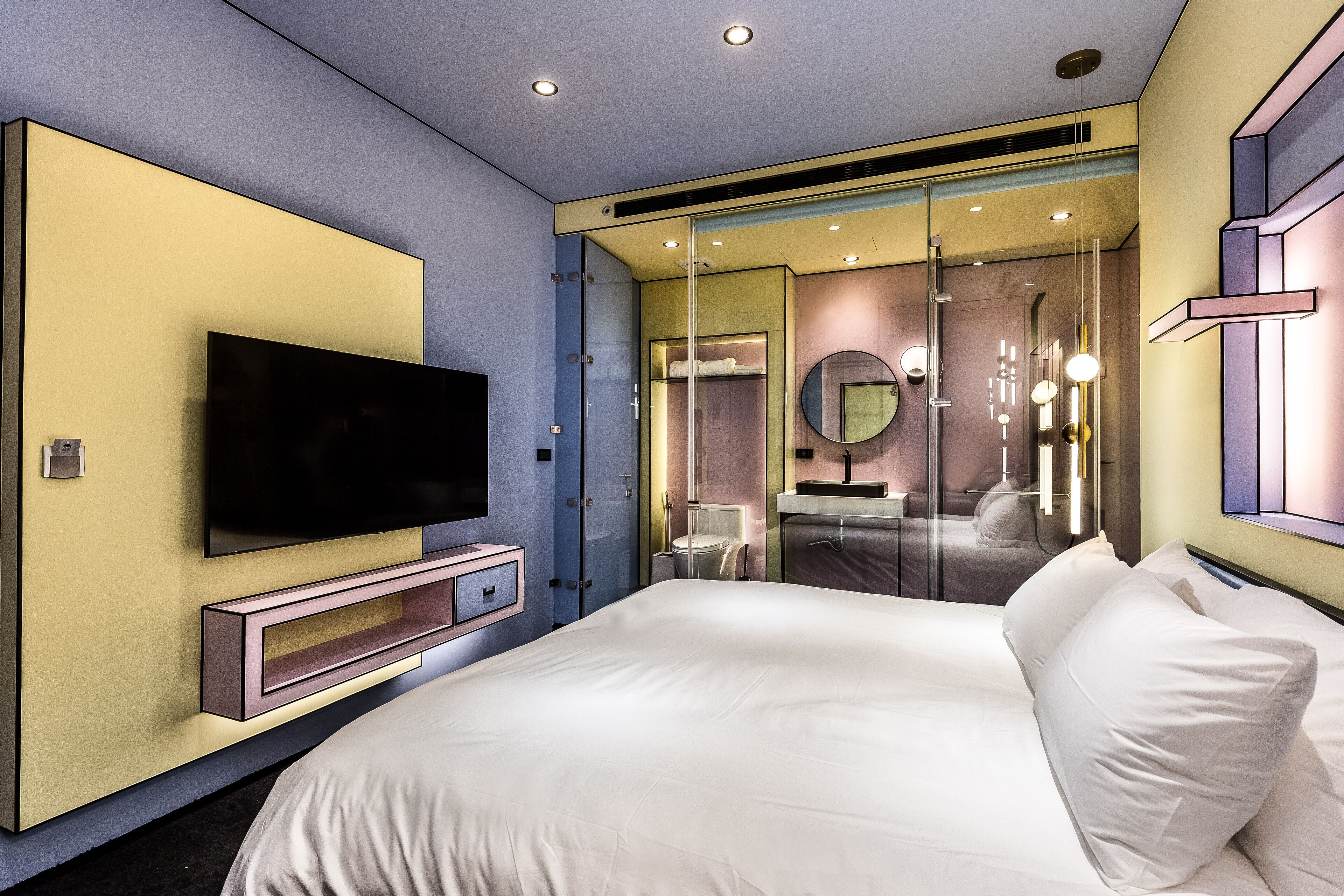 Una habitación de hotel moderna con una cama grande, un televisor de pantalla plana, un baño con mampara de cristal y un diseño minimalista.