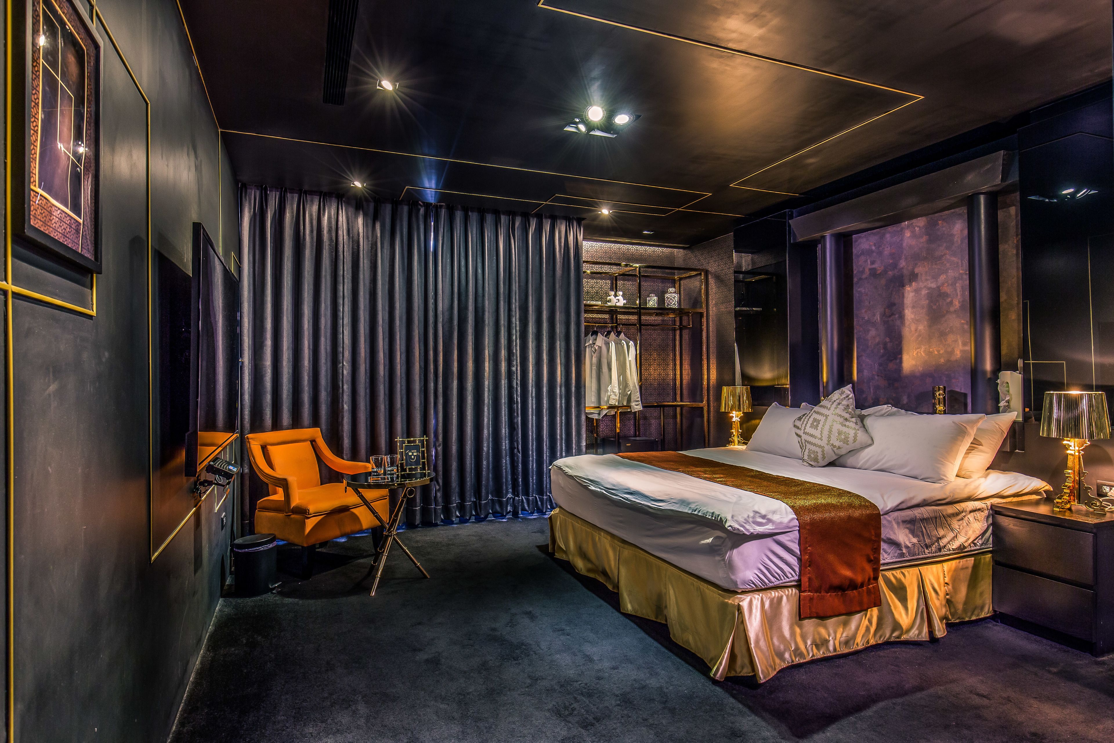 A modern hotel room with a large bed, a desk with a chair, and a wardrobe.