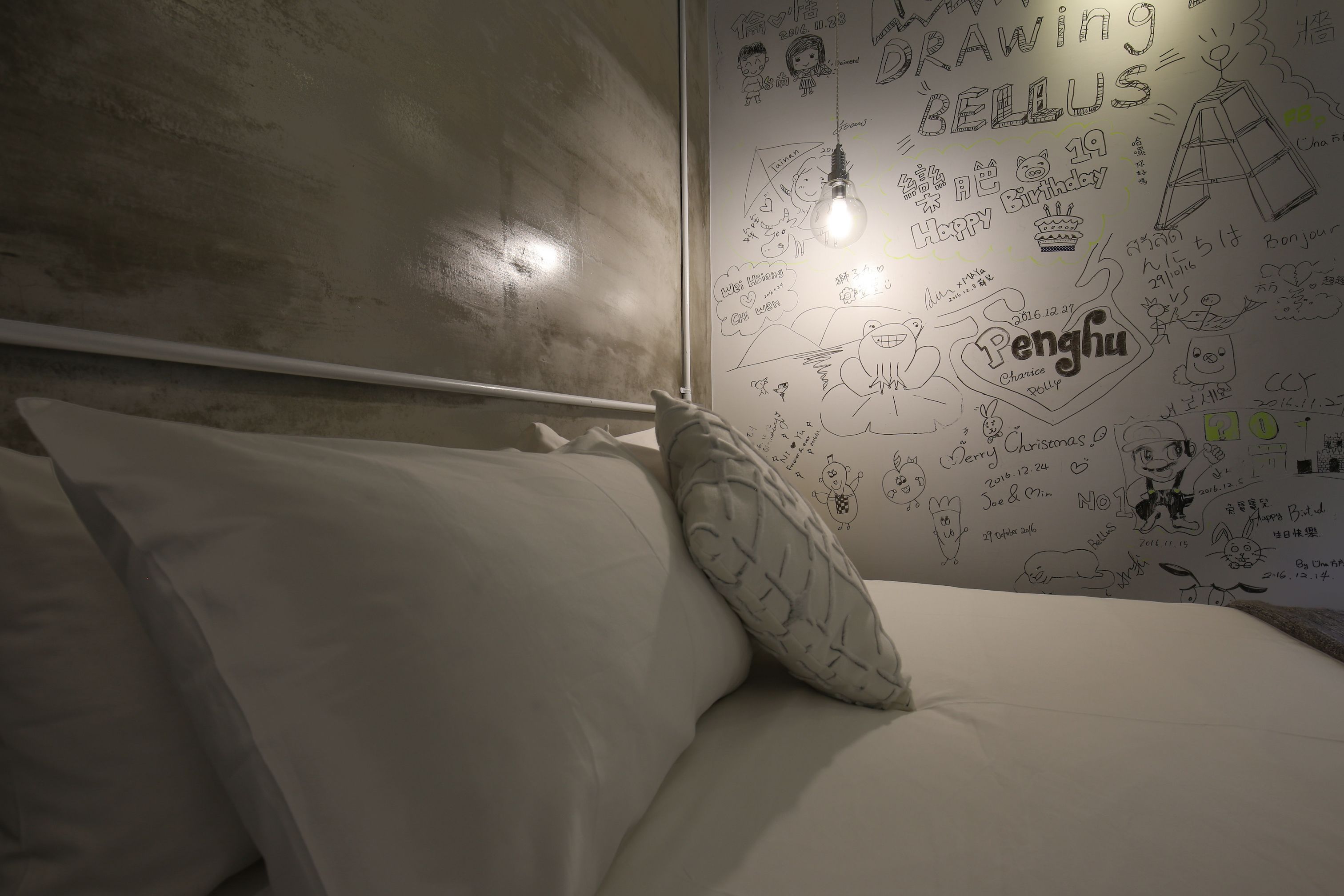 Een slaapkamer met een bed, kussens en een muur versierd met tekeningen en teksten.