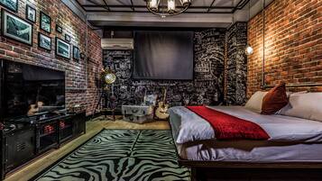 A bedroom with a brick wall, a zebra-patterned rug, a bed with white bedding and a red throw, and a guitar against the wall.