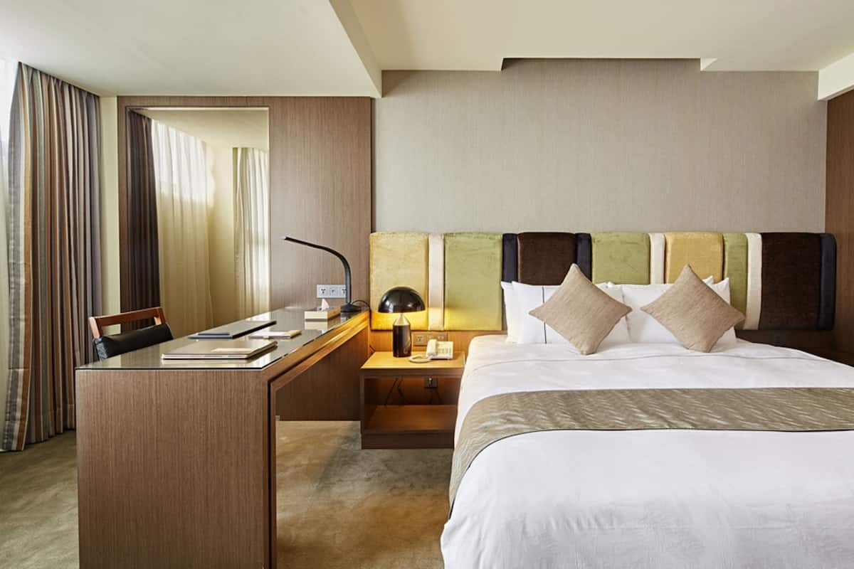 A hotel room with a bed, a desk, a chair, a lamp, and a telephone.