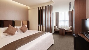 A hotel room with a large bed, a TV, a seating area, and a window with curtains. - Hotel Sukimi (Tainan)