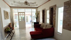 A spacious living room with a red sofa, a ceiling fan, and a view through a glass door to the outside. - I - Talay (Rayong)