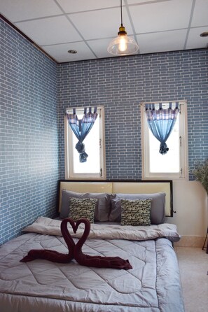 A room with a bed, two windows with curtains, a hanging light fixture, and a wall with a blue brick pattern. - I - Talay (Rayong)