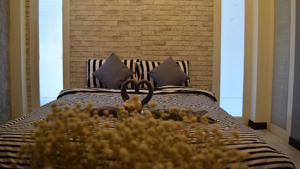A bedroom with a brick wall, a zebra-striped bedspread, and two pillows. - I - Talay (Rayong)
