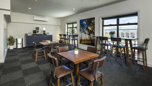 Un comedor moderno con varias mesas y sillas, una cocina al fondo y ventanas amplias con vistas al exterior.