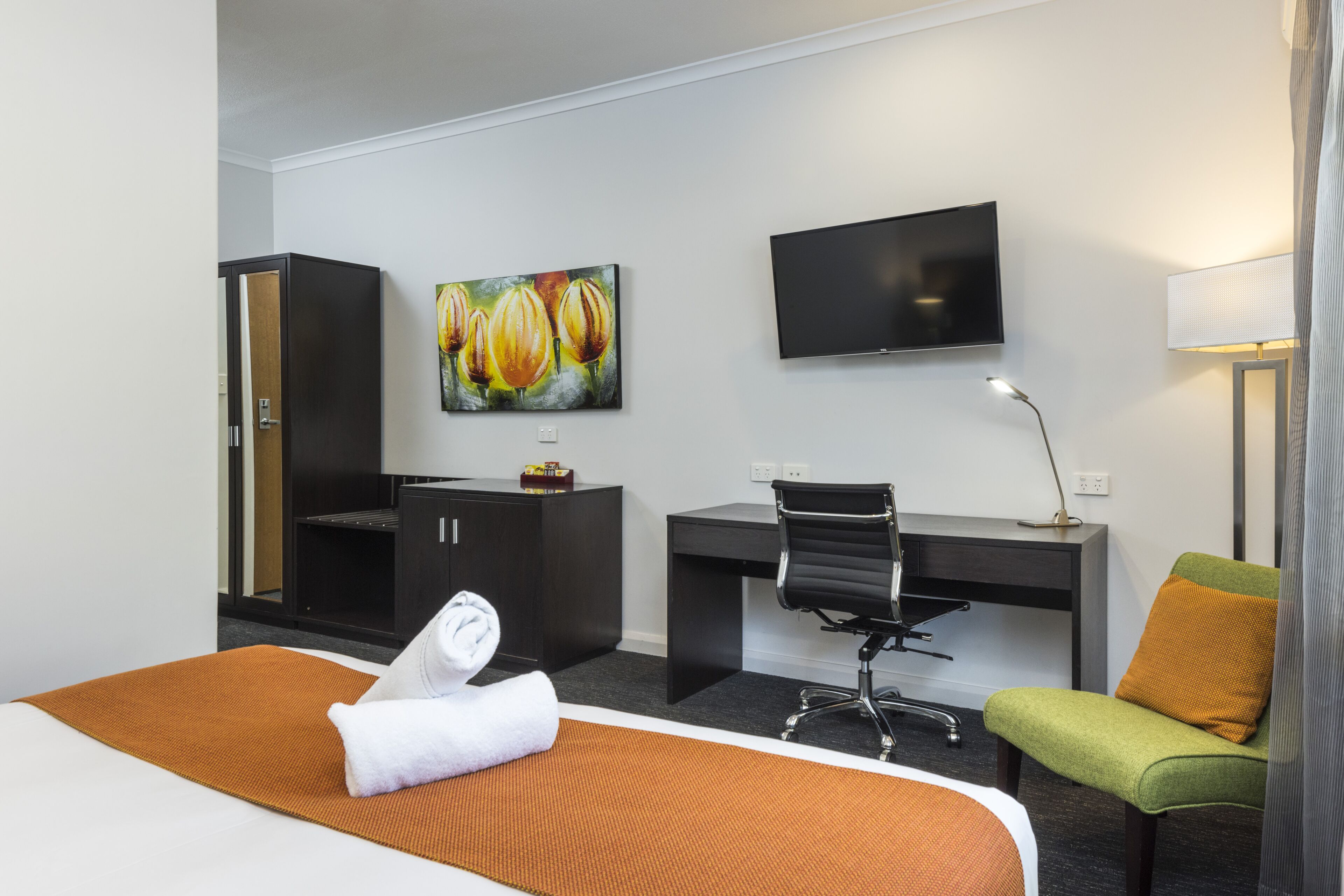 Ein Hotelzimmer mit Bett, Schreibtisch, Sessel, Fernseher und einem Bild an der Wand.