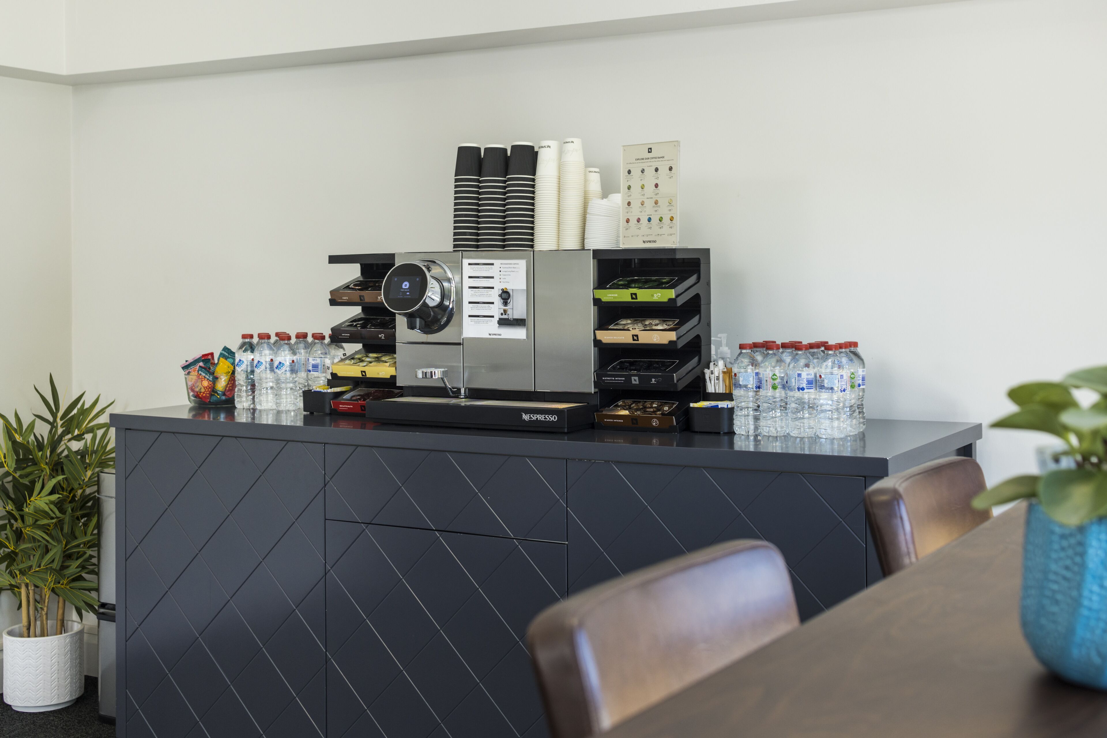 Un comptoir d’accueil moderne, équipé d’une machine à café, de bouteilles d’eau et d’un tableau affichant le menu.