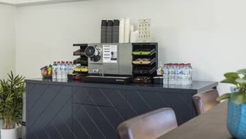 Un comptoir d’accueil moderne, équipé d’une machine à café, de bouteilles d’eau et d’un tableau affichant le menu.