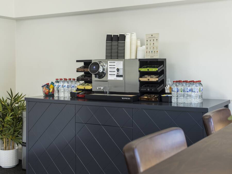 Un comptoir d’accueil moderne, équipé d’une machine à café, de bouteilles d’eau et d’un tableau affichant le menu.