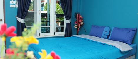 A bedroom with a blue bedspread, two pillows, a nightstand, and a window with curtains.