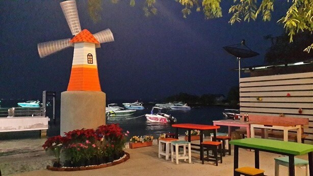 Un moulin à vent, des bateaux et des tables pour s’asseoir à l’extérieur, au bord de l’eau.