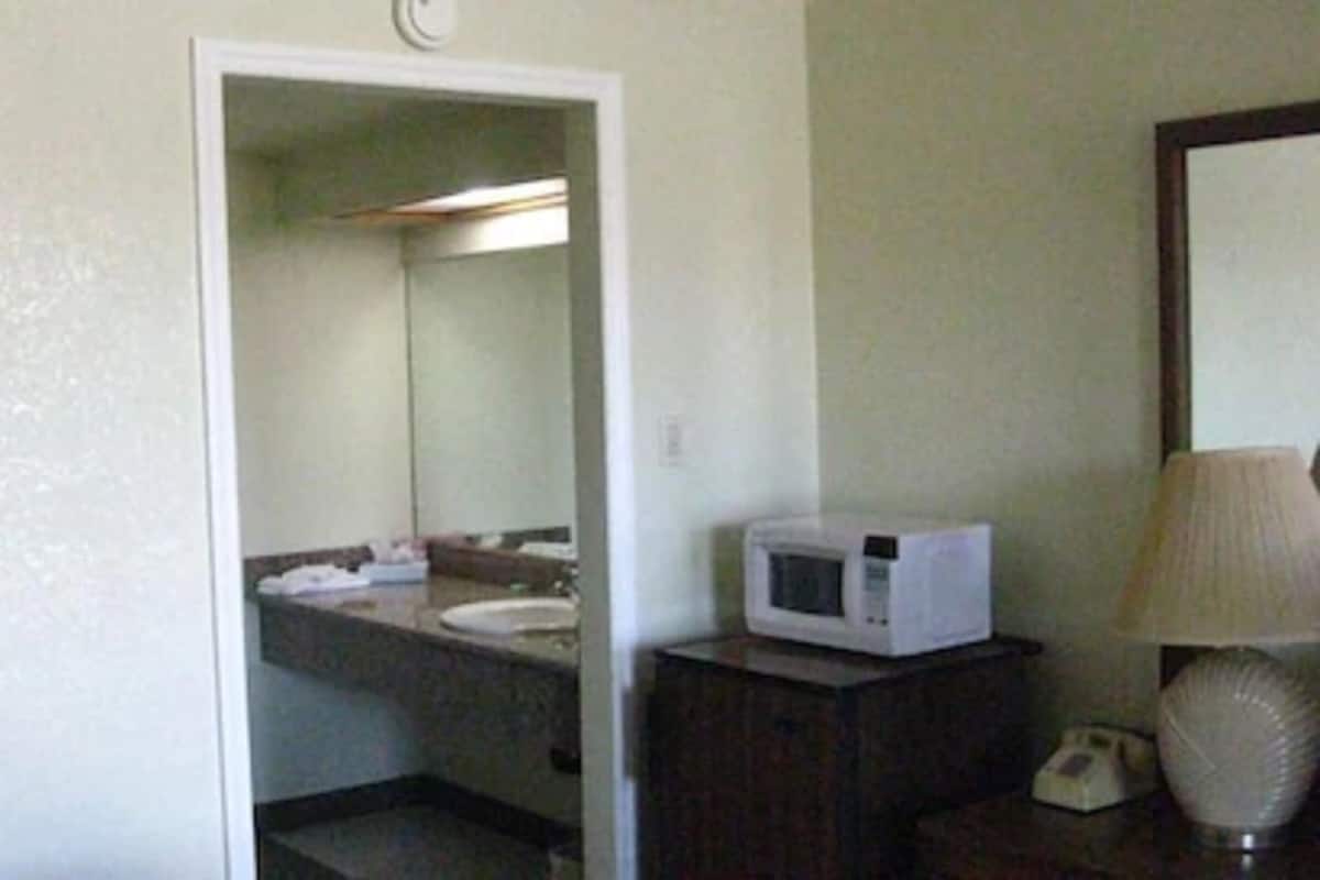Un baño con lavamanos, espejo, microondas y teléfono.