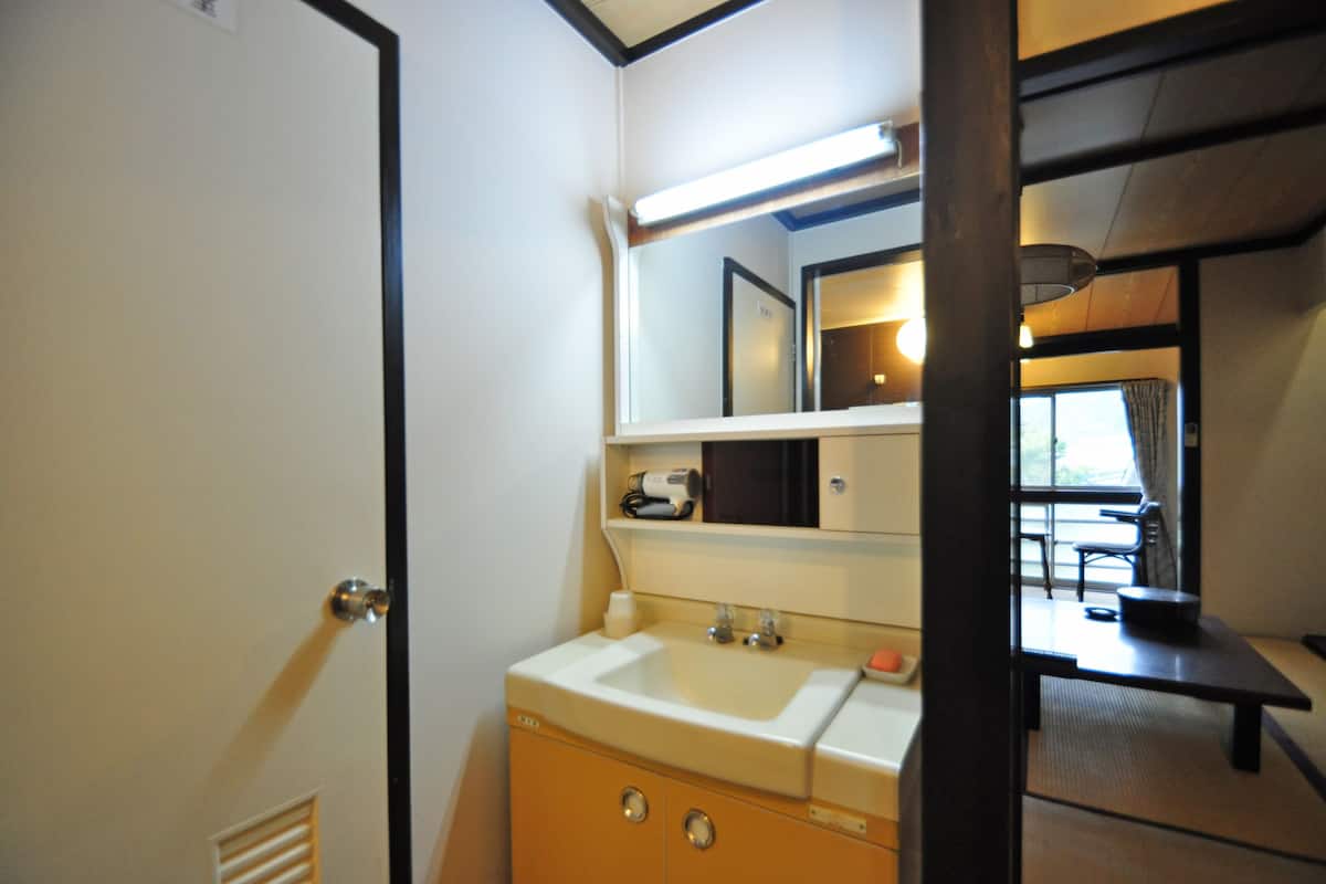 A compact bathroom with a sink, mirror, and a small table with a chair.