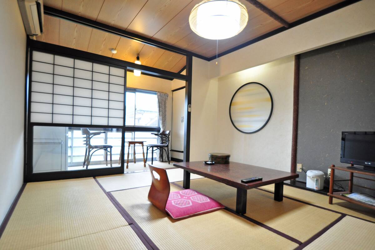 A traditional Japanese room with tatami flooring, a low table, a television, and a sliding door leading to another room.