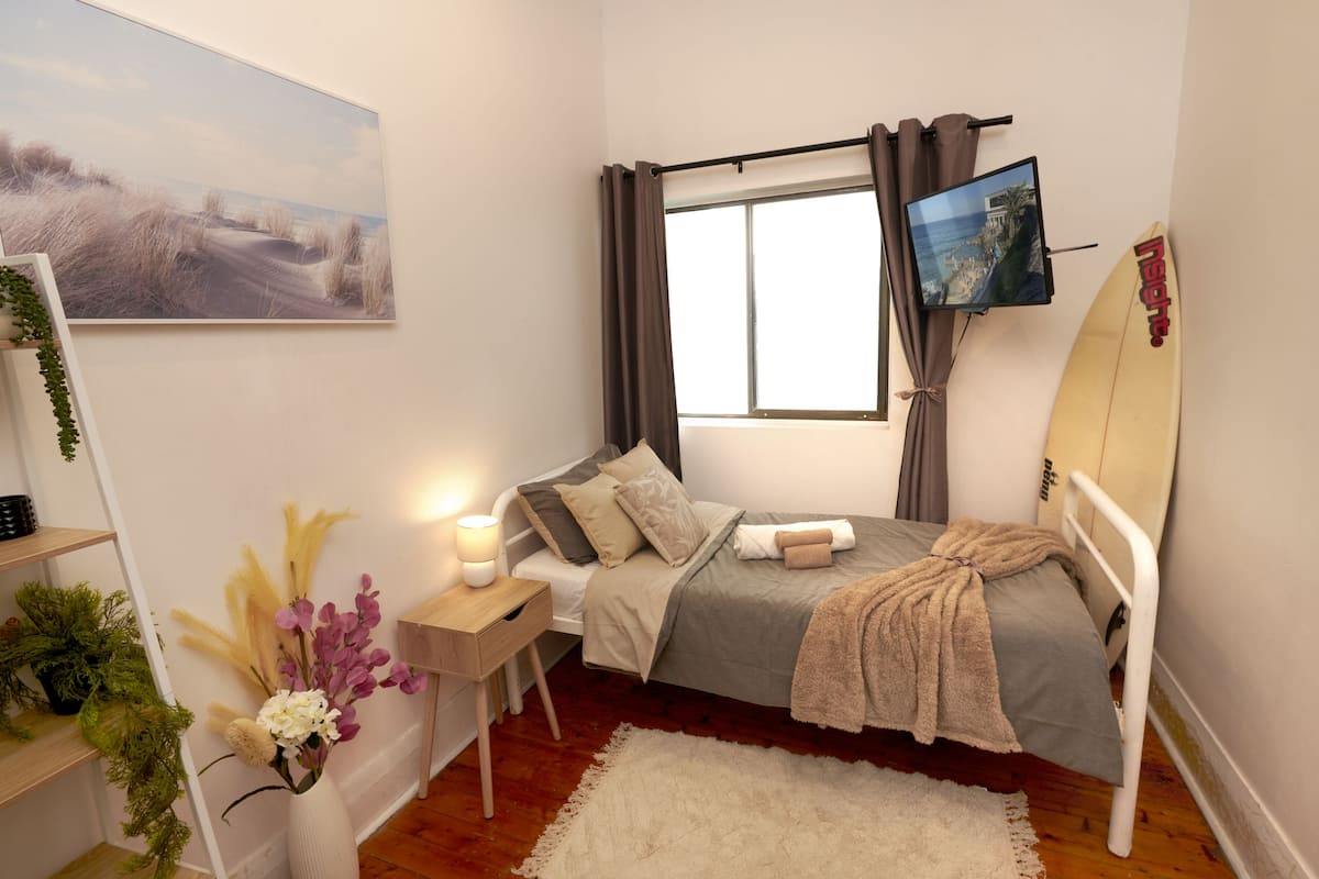 A bedroom with a bed, a TV, a surfboard, and a painting.