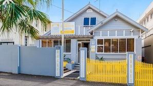 A two-story building with a grey facade, a blue gate, and a yellow fence. - Coogee Beachside - Hostel (Coogee)