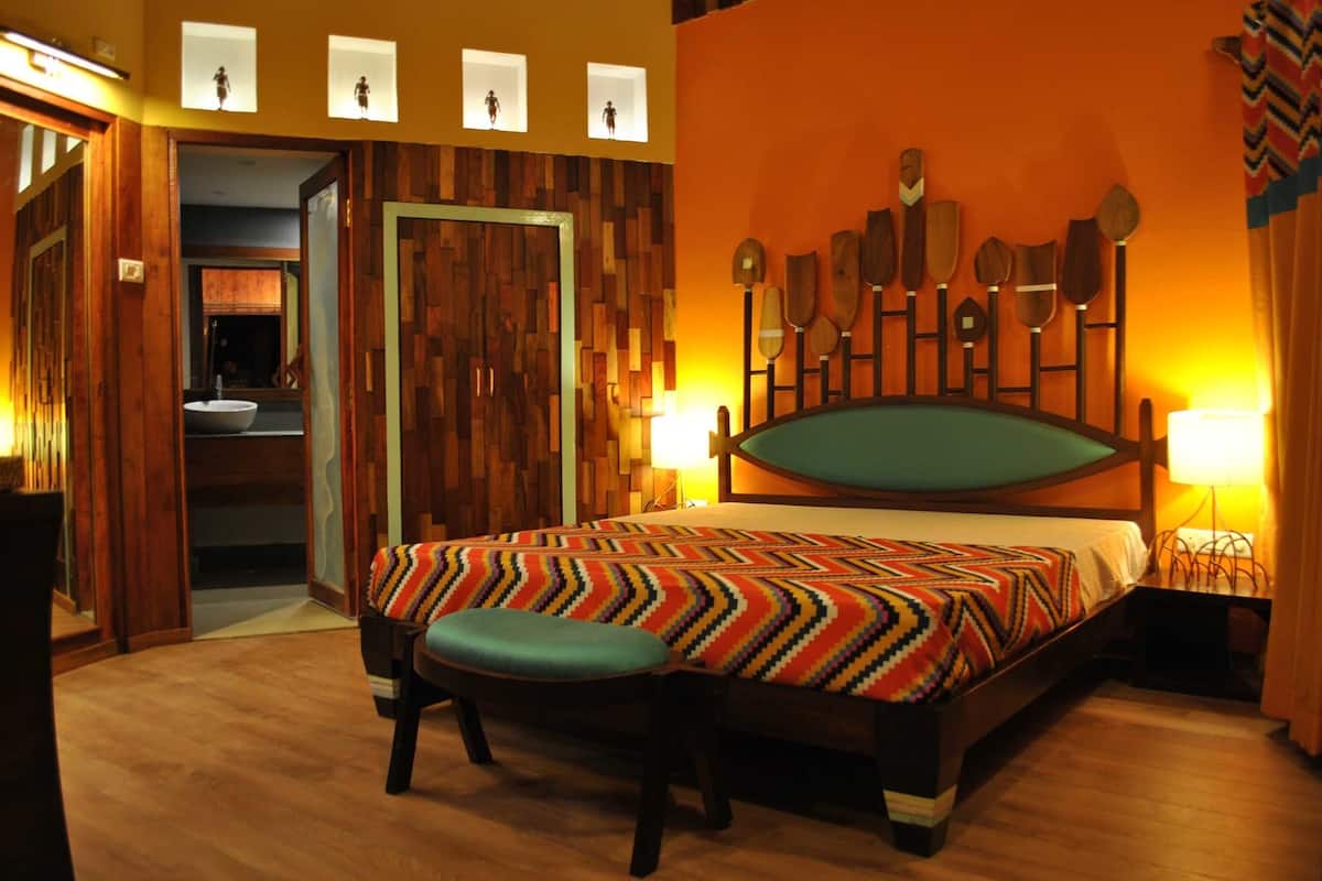 A room with a bed, a bench, a wooden wall, and a mirror.