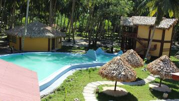 Relax by the pool surrounded by lush greenery and palm trees in a serene tropical setting.