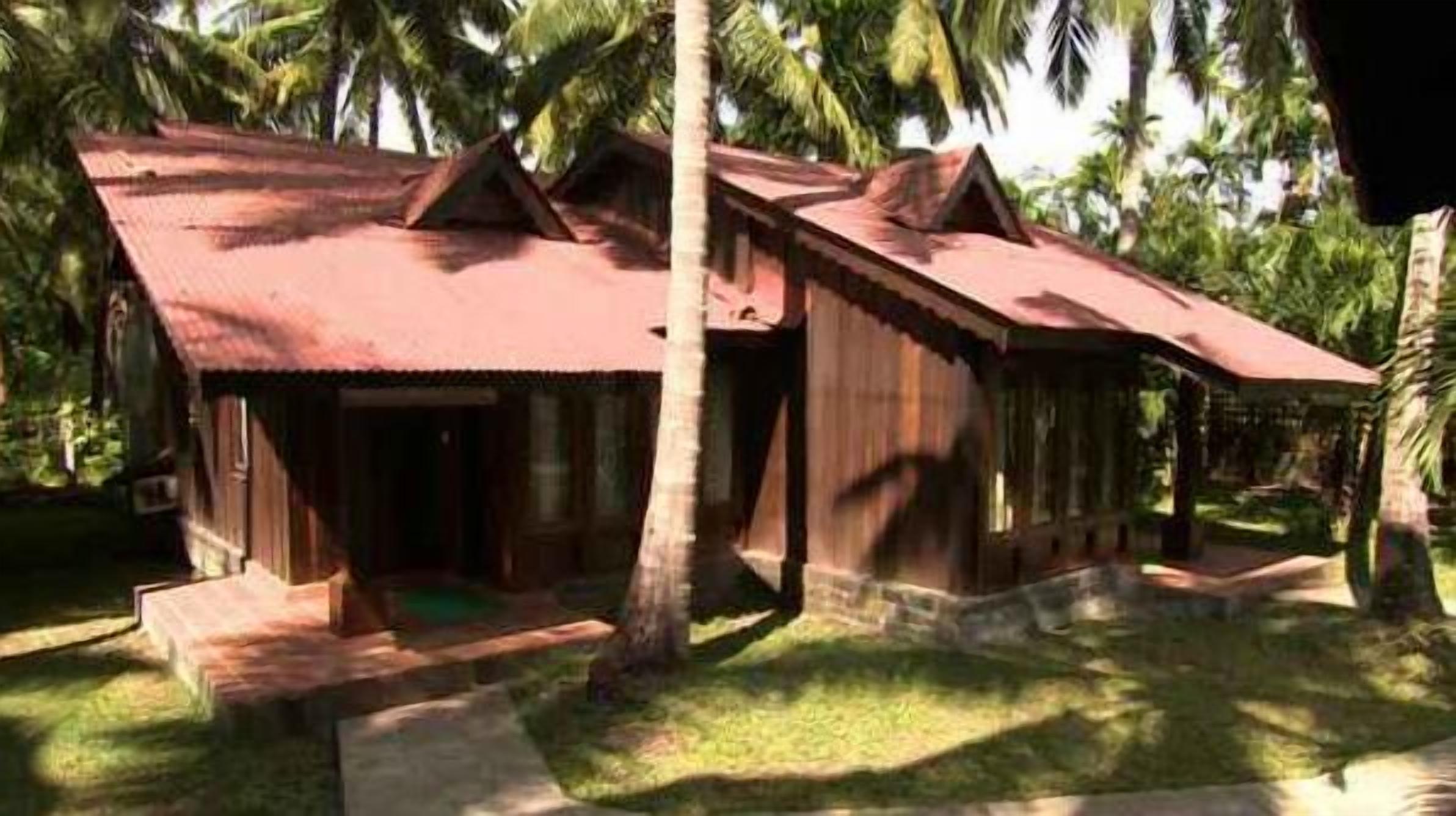 A wooden house with a red roof, surrounded by palm trees.