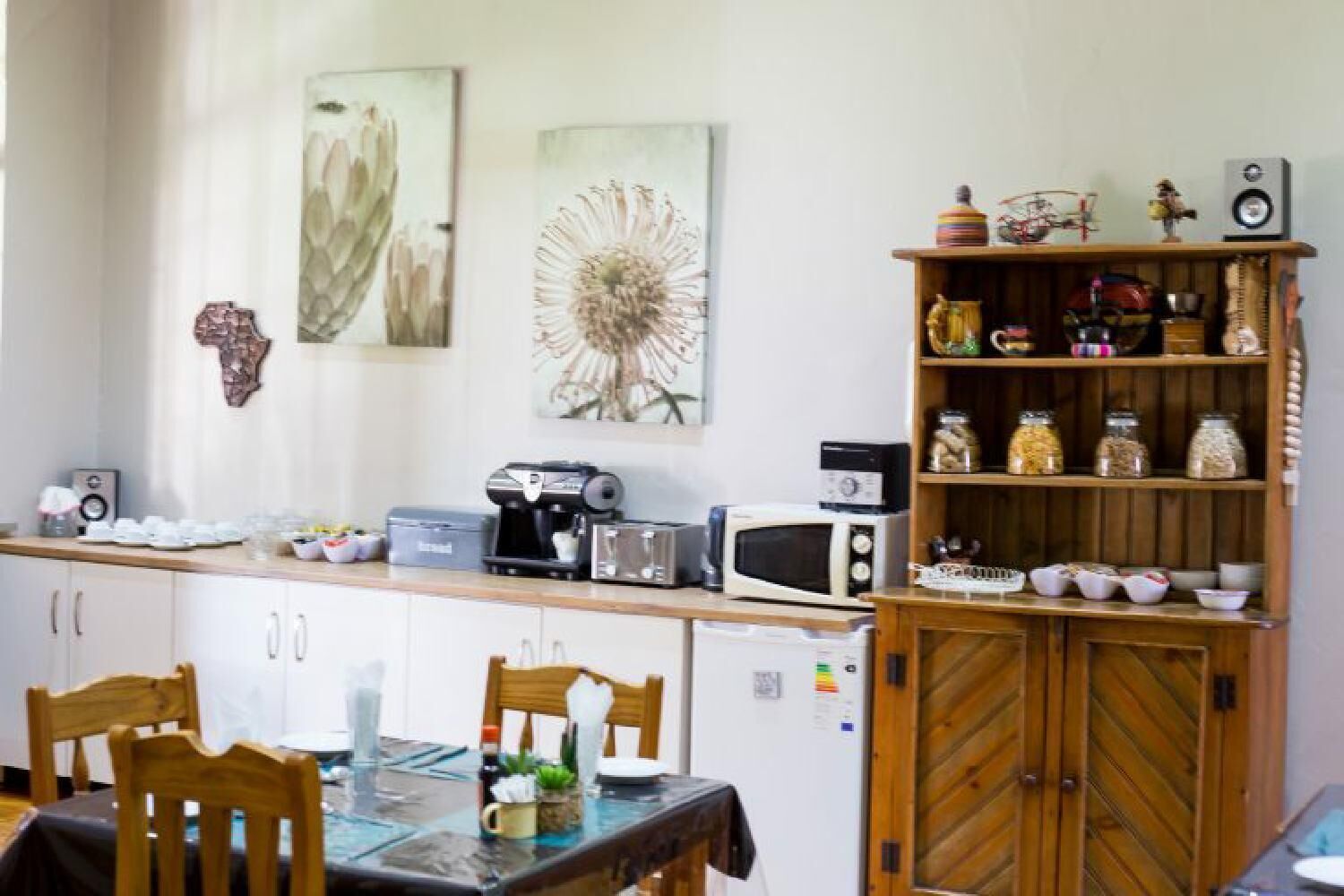 Una cocina con armarios de madera, una mesa de comedor con sillas, una cafetera, un microondas y un estante con frascos y una bicicleta.