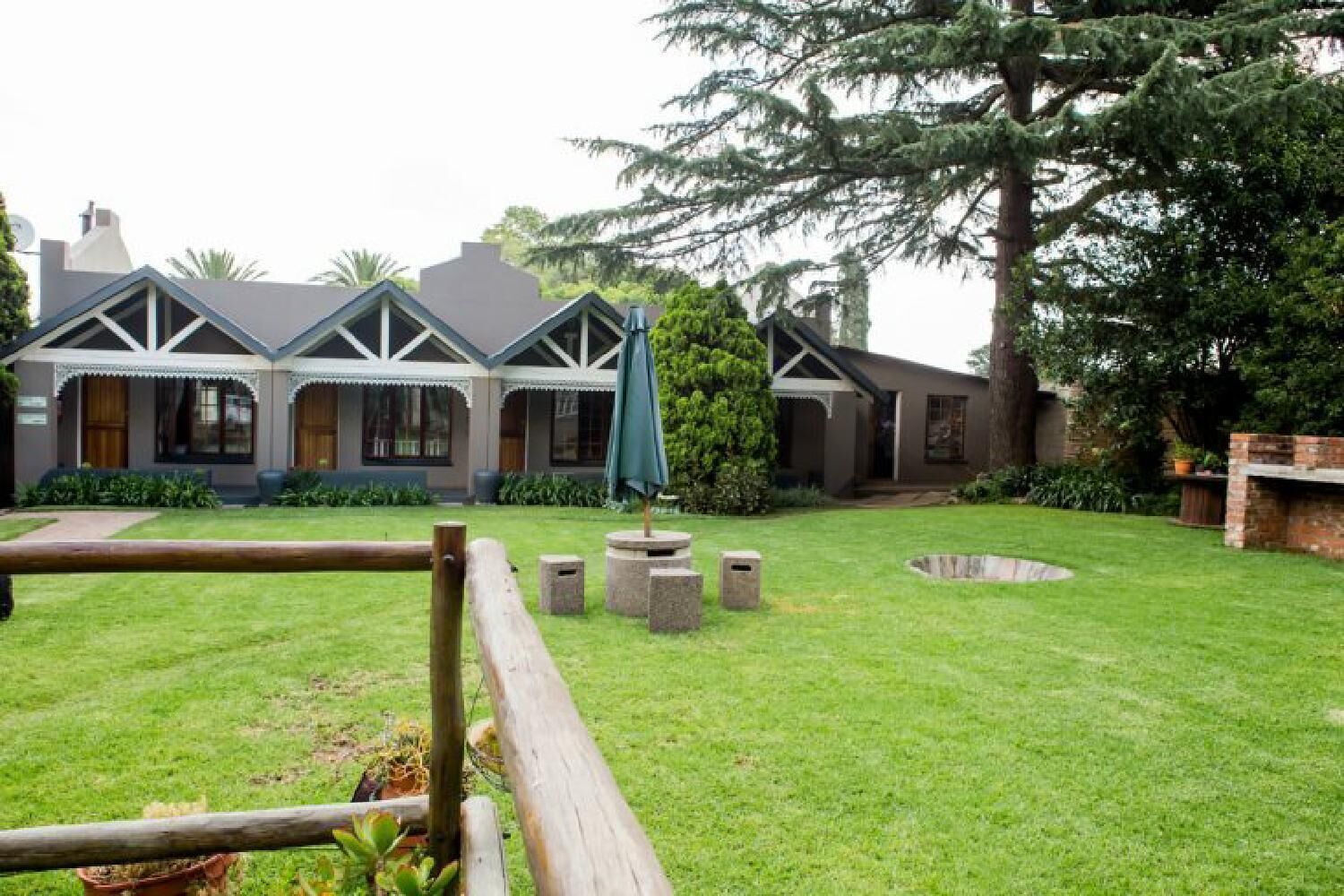 Una casa con césped cuidado, cerca de madera y un gran árbol.