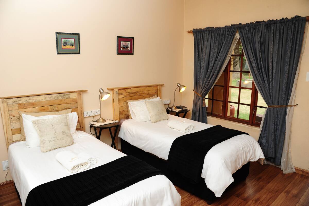 A hotel room with two beds, wooden headboards, bedside lamps, and a window with curtains.