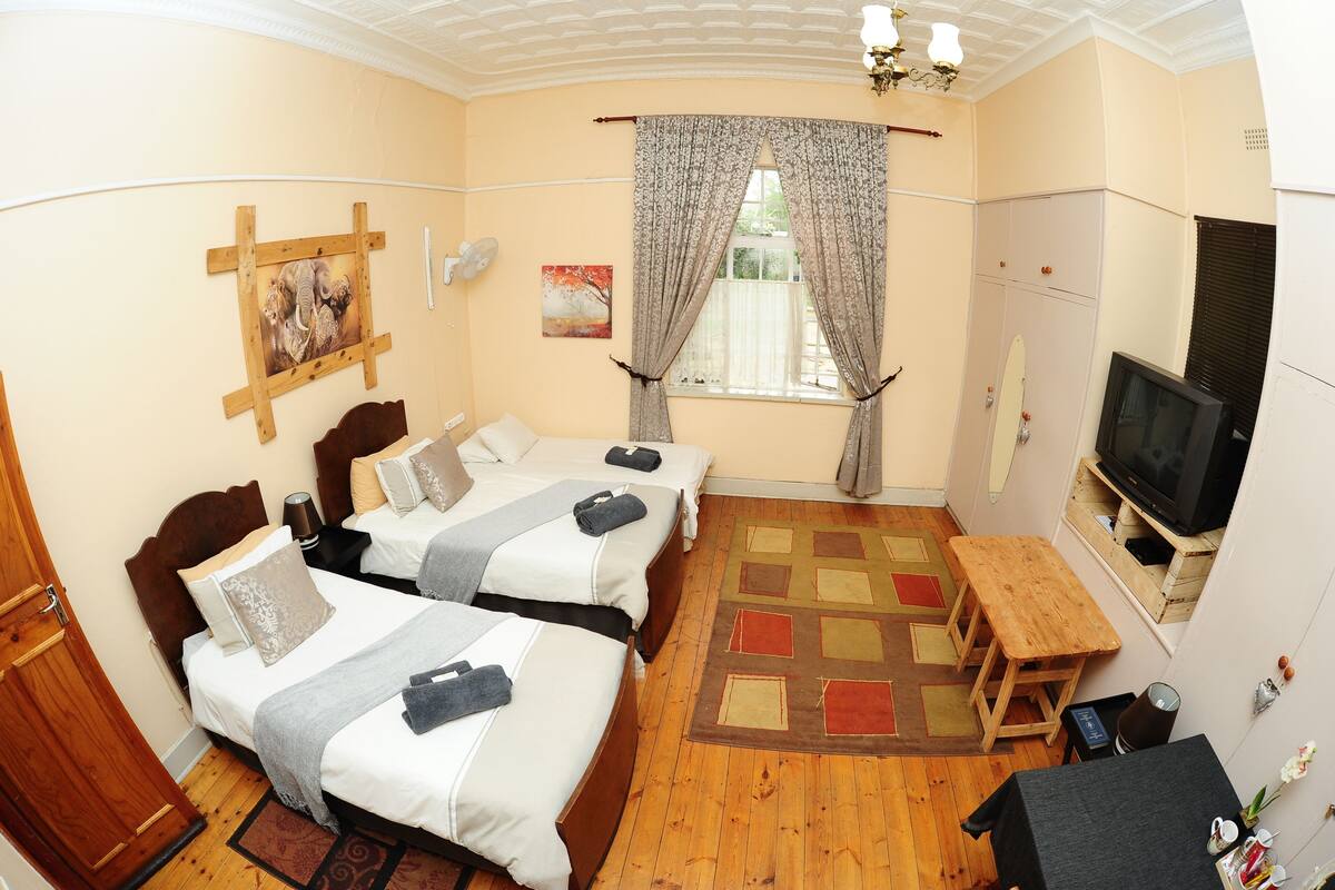 A hotel room with two beds, a TV, a wooden bench, and a window with curtains.