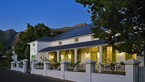 Un edificio blanco con balcón, paneles solares y montañas al fondo.