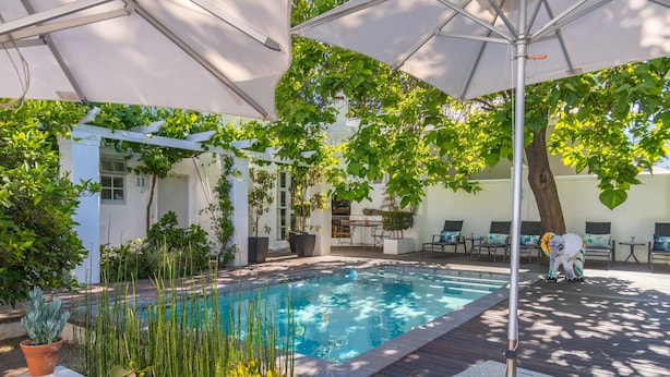 Una piscina con cubierta de madera, rodeada de plantas en macetas y un pérgola.
