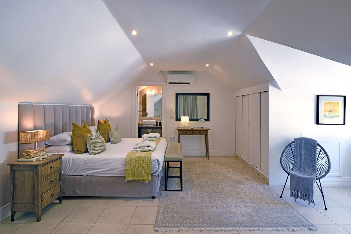 Un dormitorio con cama, mesita de noche, banco, silla y un escritorio pequeño con espejo.