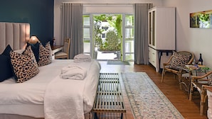 Un dormitorio con una cama grande, un escritorio y vista a un jardín por una puerta abierta.