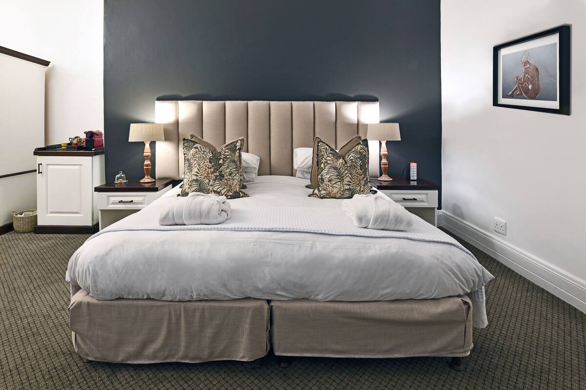 Habitación de hotel con una cama grande, una mesita de noche con lámpara, una pequeña mesa con lámpara y un cuadro en la pared.