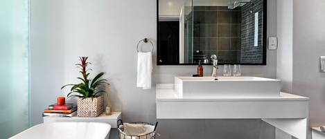 A modern bathroom with a large mirror, two sinks, a bathtub, and a potted plant.